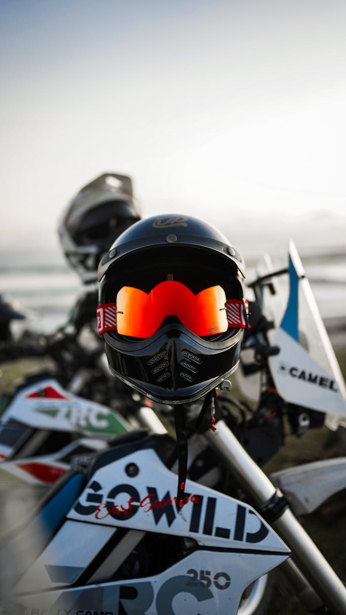 Close-up of a striking motorcycle helmet mounted on off-road bikes against a clear sky backdrop.