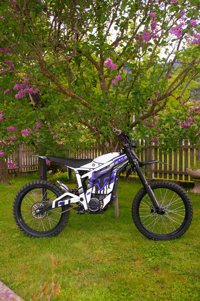 A sleek electric dirt bike parked in a lush green garden with blooming flowers.