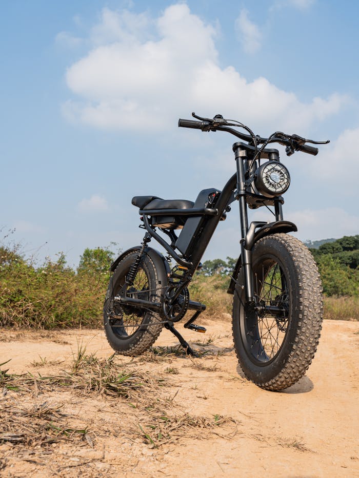 A black fat tire electric bike parked on a dirt path in a natural setting under a clear blue sky.