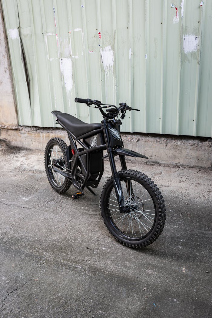 Electric dirt bike parked against industrial background on urban street.