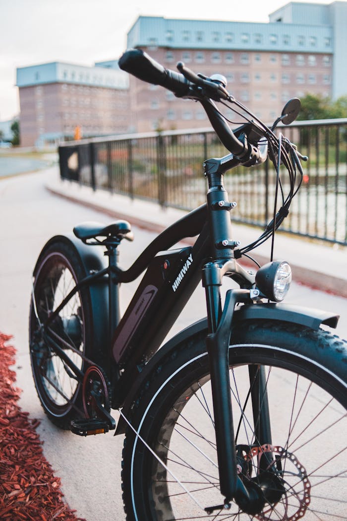 Close-up of a black electric bicycle parked on a city pathway near modern buildings.