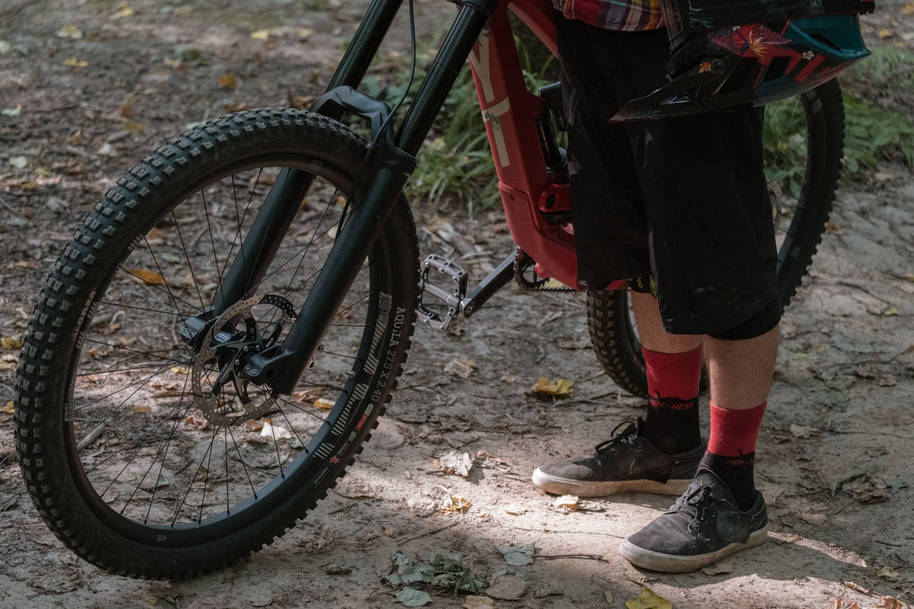 Close-up of a mountain biker standing on a dirt trail with gear and bike.